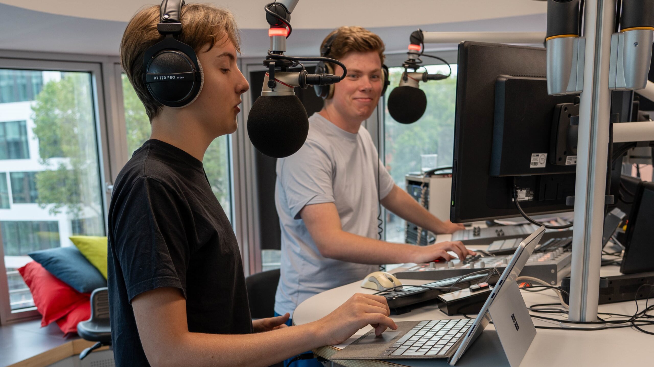 Zwei Männer moderieren gemeinsam in einem Hörfunkstudio.