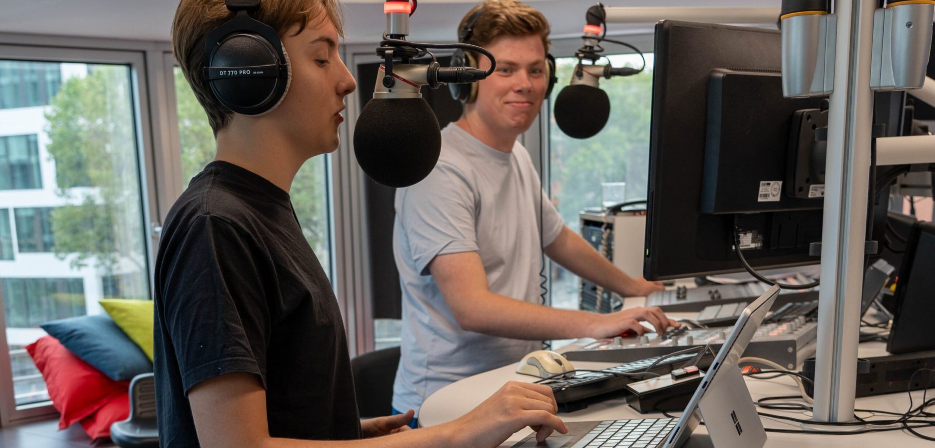 Zwei Männer moderieren gemeinsam in einem Hörfunkstudio.
